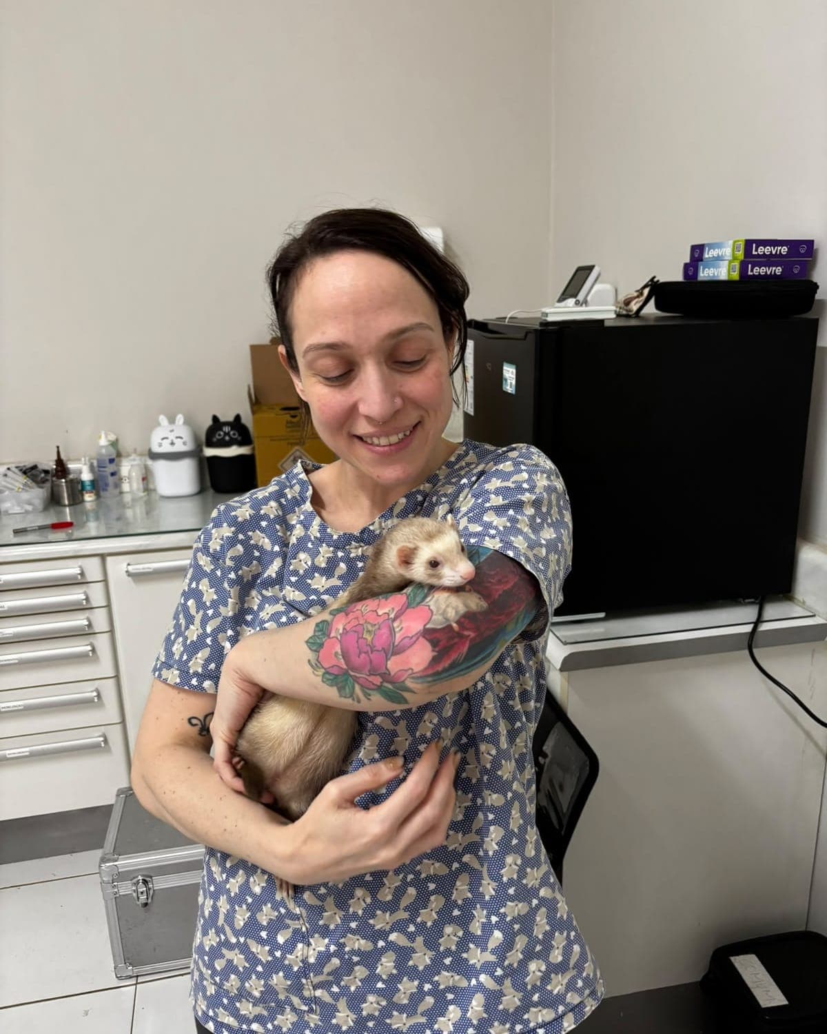 Dra. Mariana Bizzo segurando um furão de pelo claro no colo, sorrindo pra ele, na sala de procedimentos
