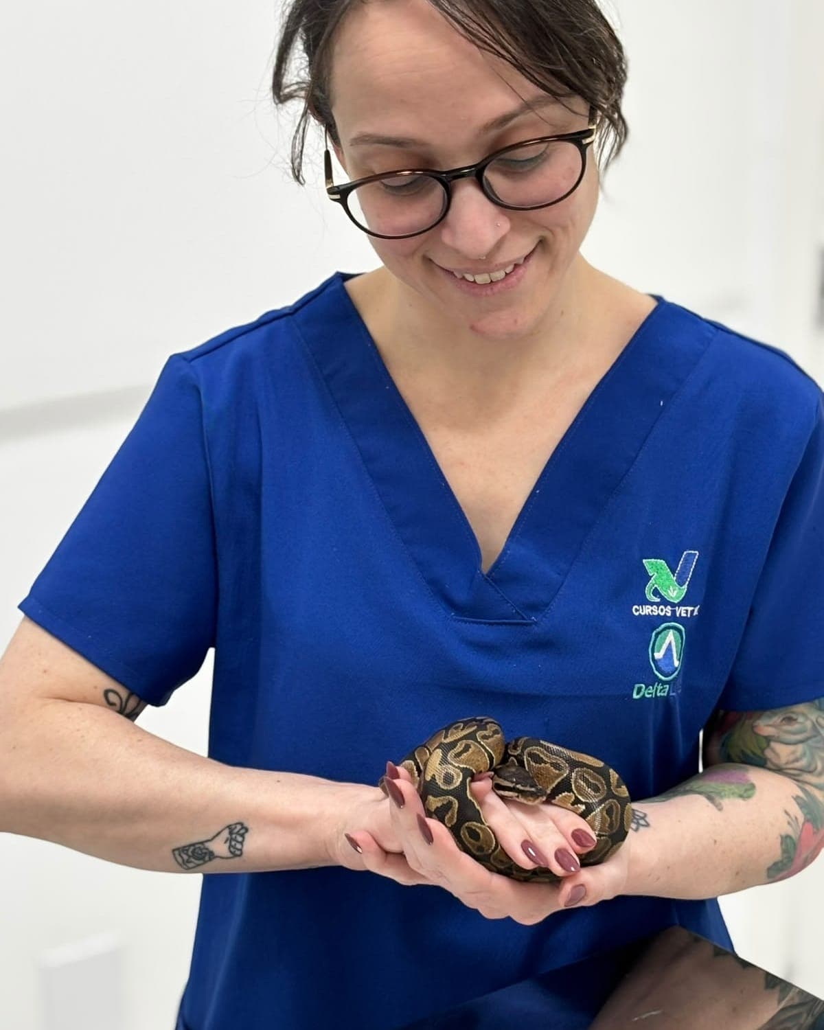 Dra. Mariana Bizzo, de jaleco azul, sorrindo com uma serpente píton-bola enrolada nas mãos